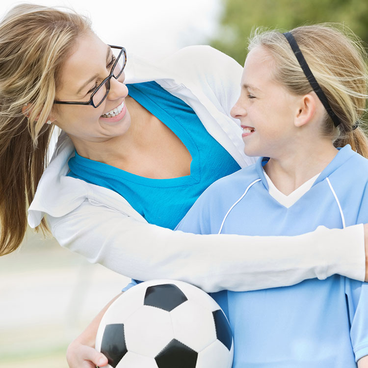 Girl with soccer ball embraced and smiling with older woman