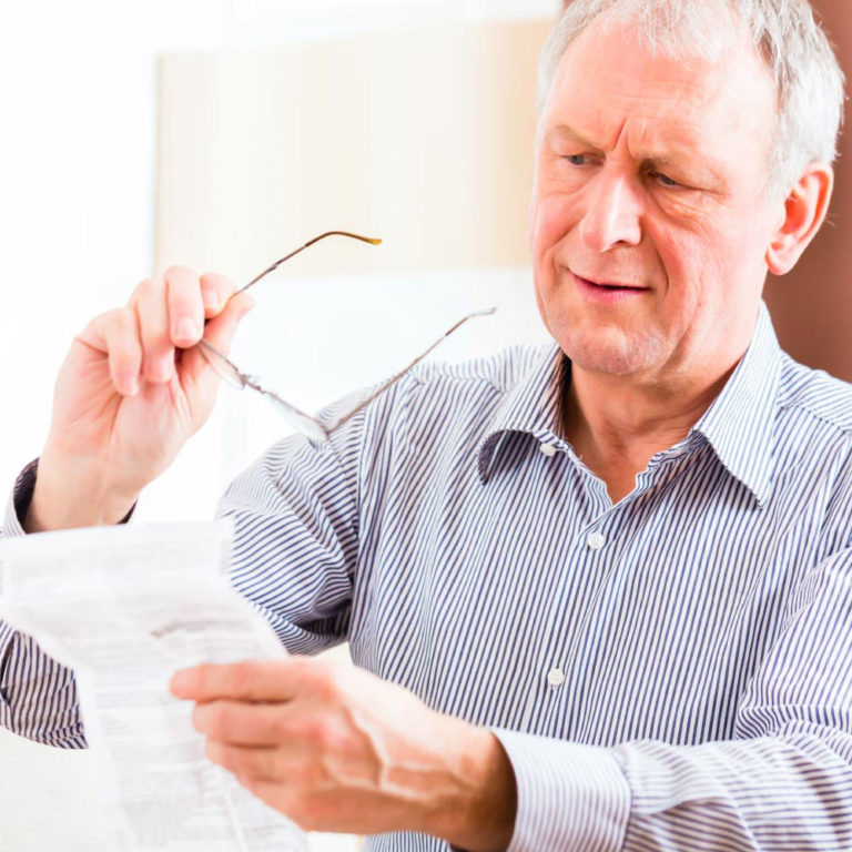 Older man holding glasses looking confused at papers