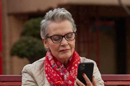 Older woman with glasses using smartphone while sitting on a bench